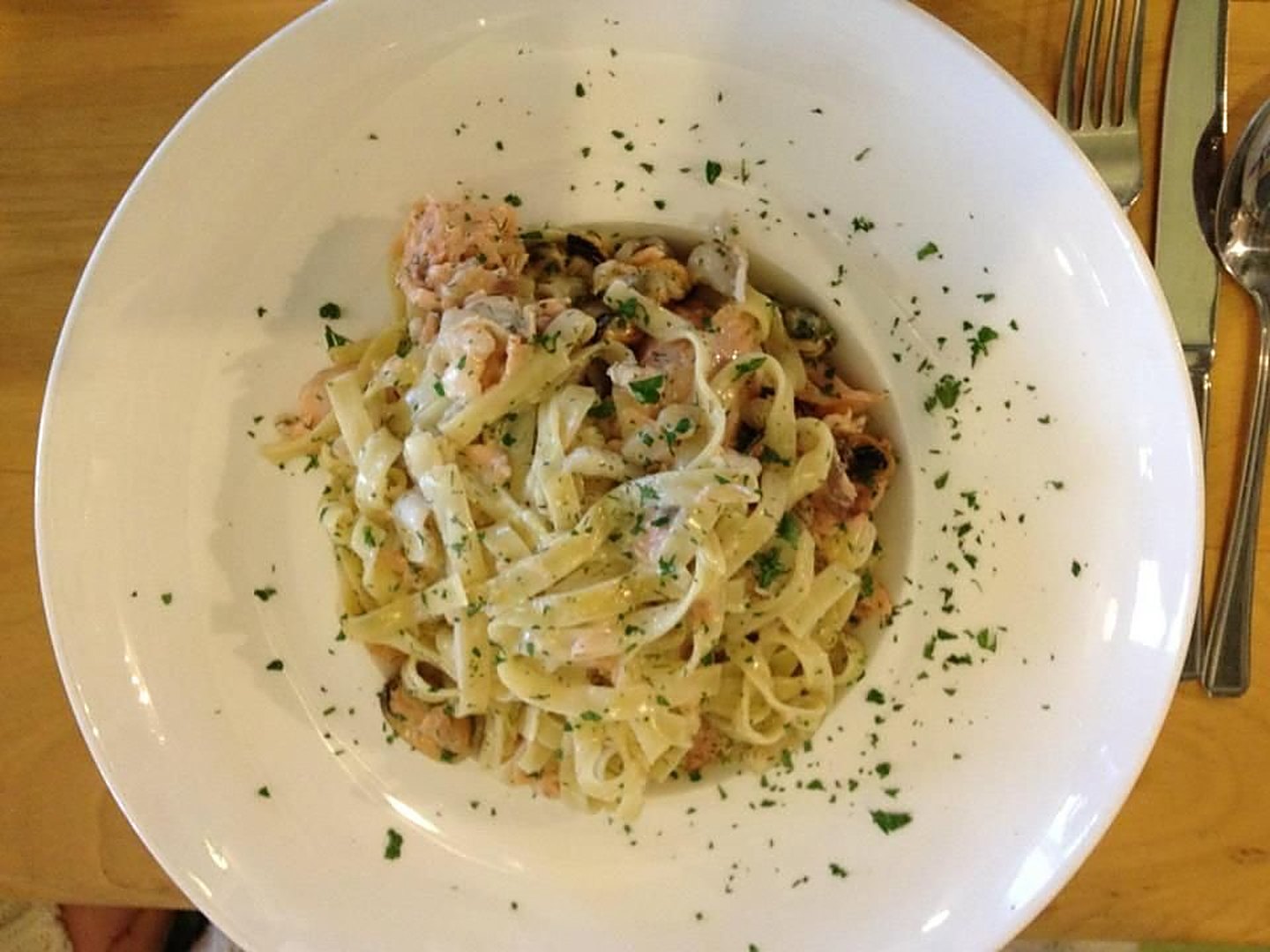 A white bowl of ribbon pasta in a creamy sauce, scattered with parsley